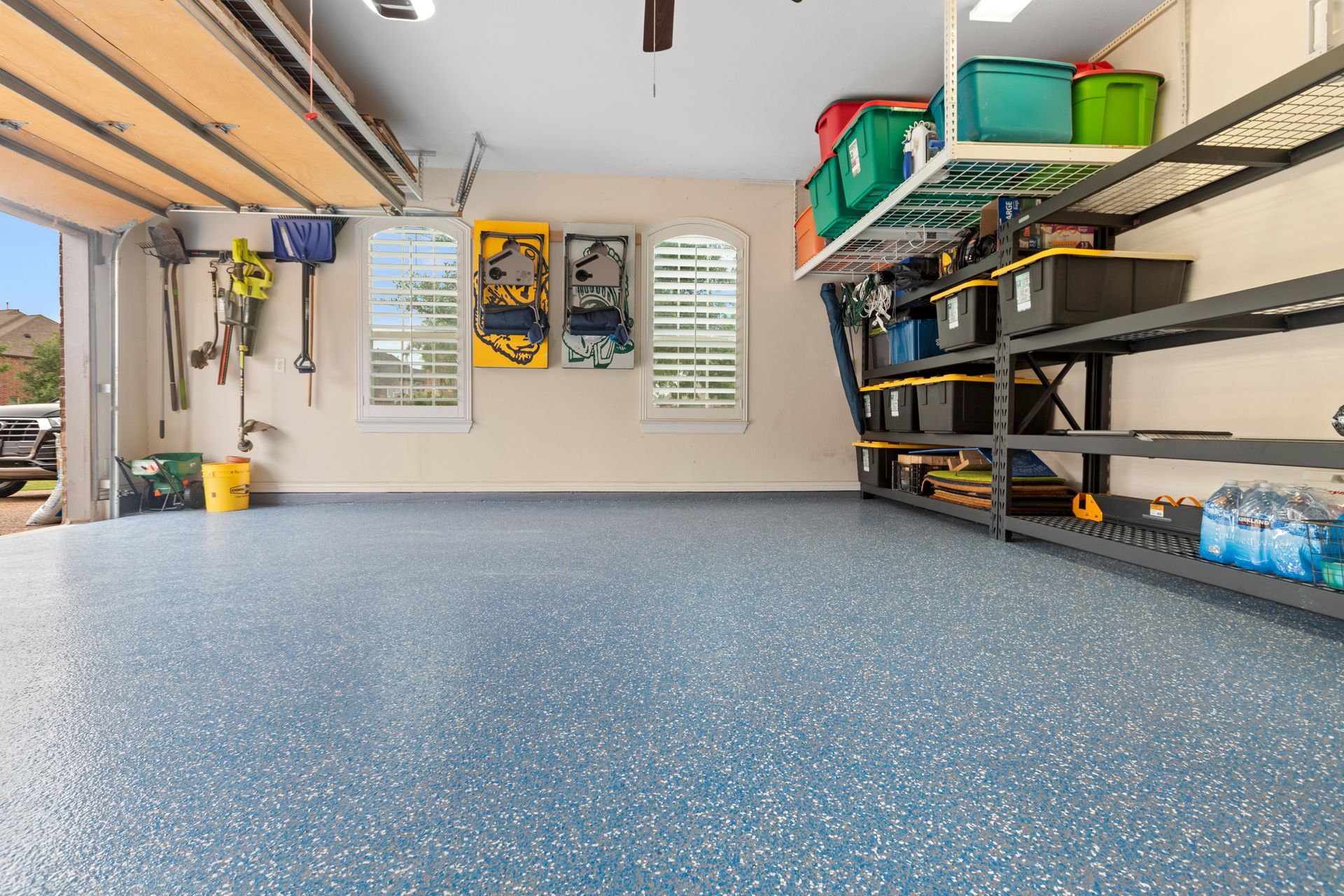 Clean garage with blue speckled floor, shelving, storage bins, and an open garage door.