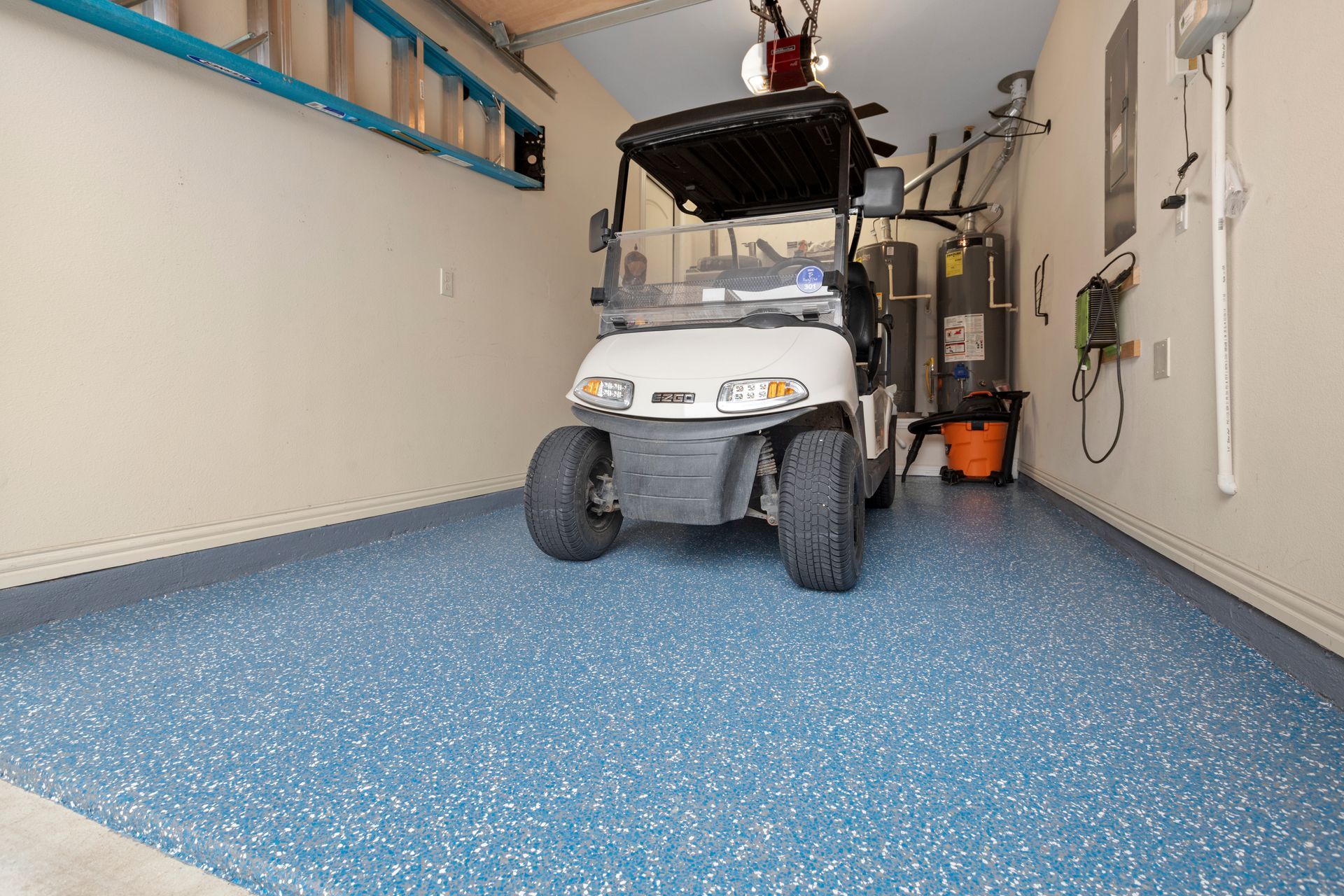 White golf cart in a garage with blue speckled floor and storage shelves along the walls