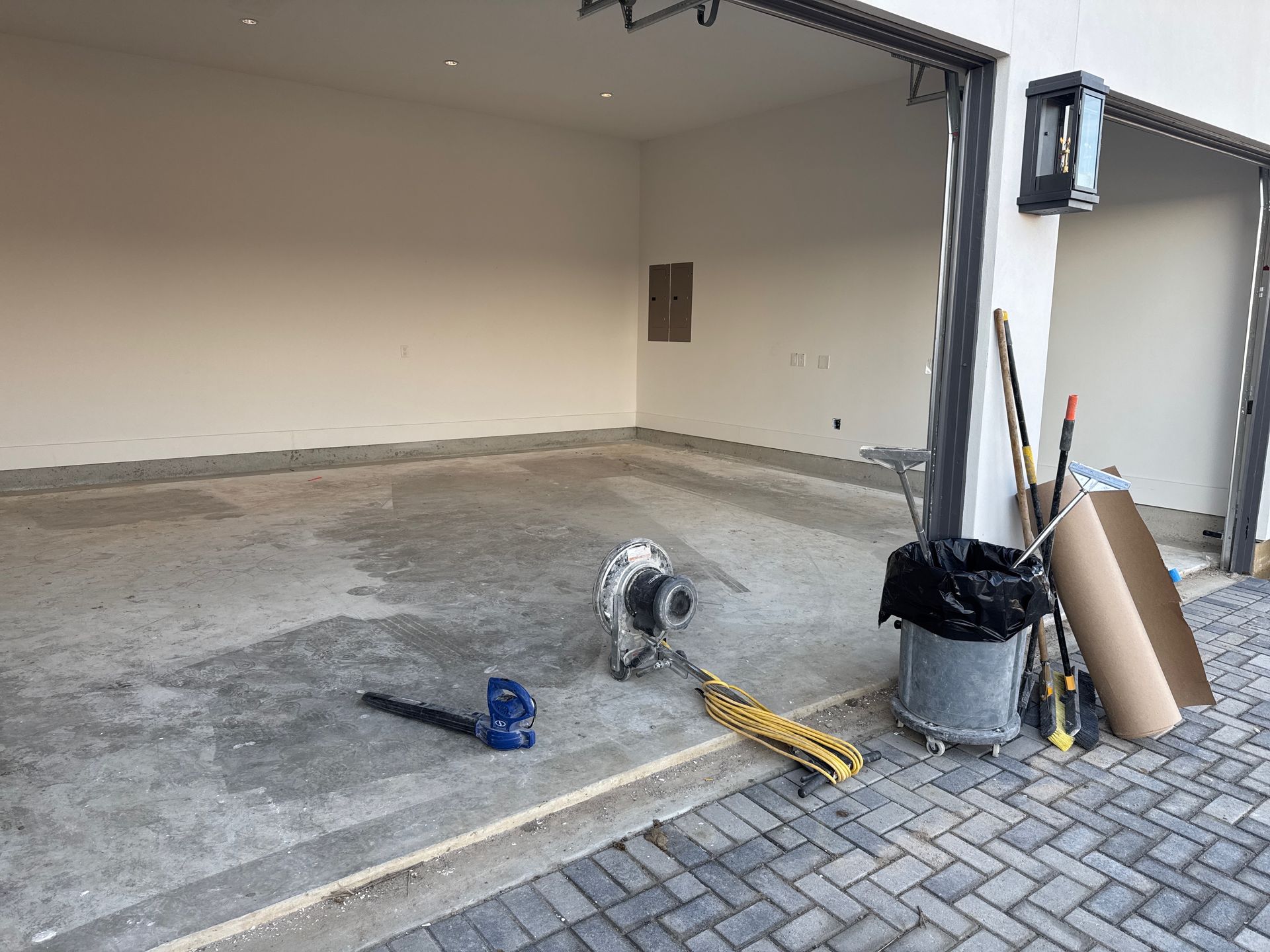 Empty garage with concrete floor, tools, and cleaning supplies near the entrance.
