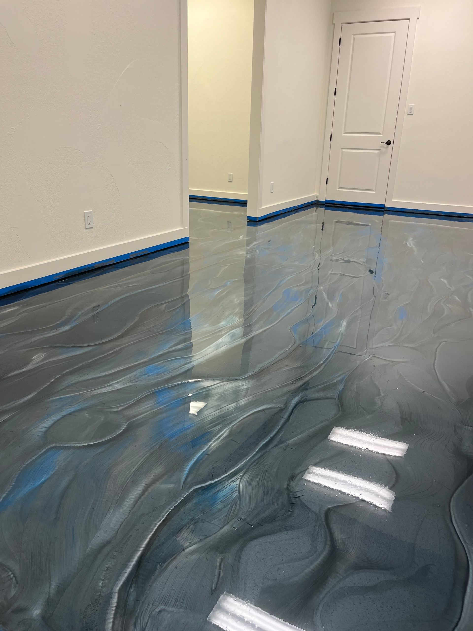 Empty room with glossy blue floor covering and white walls, reflecting ceiling lights.