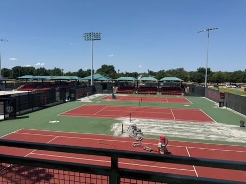 Outdoor tennis courts with green and red surfaces, netting, and stadium lights under a clear sky