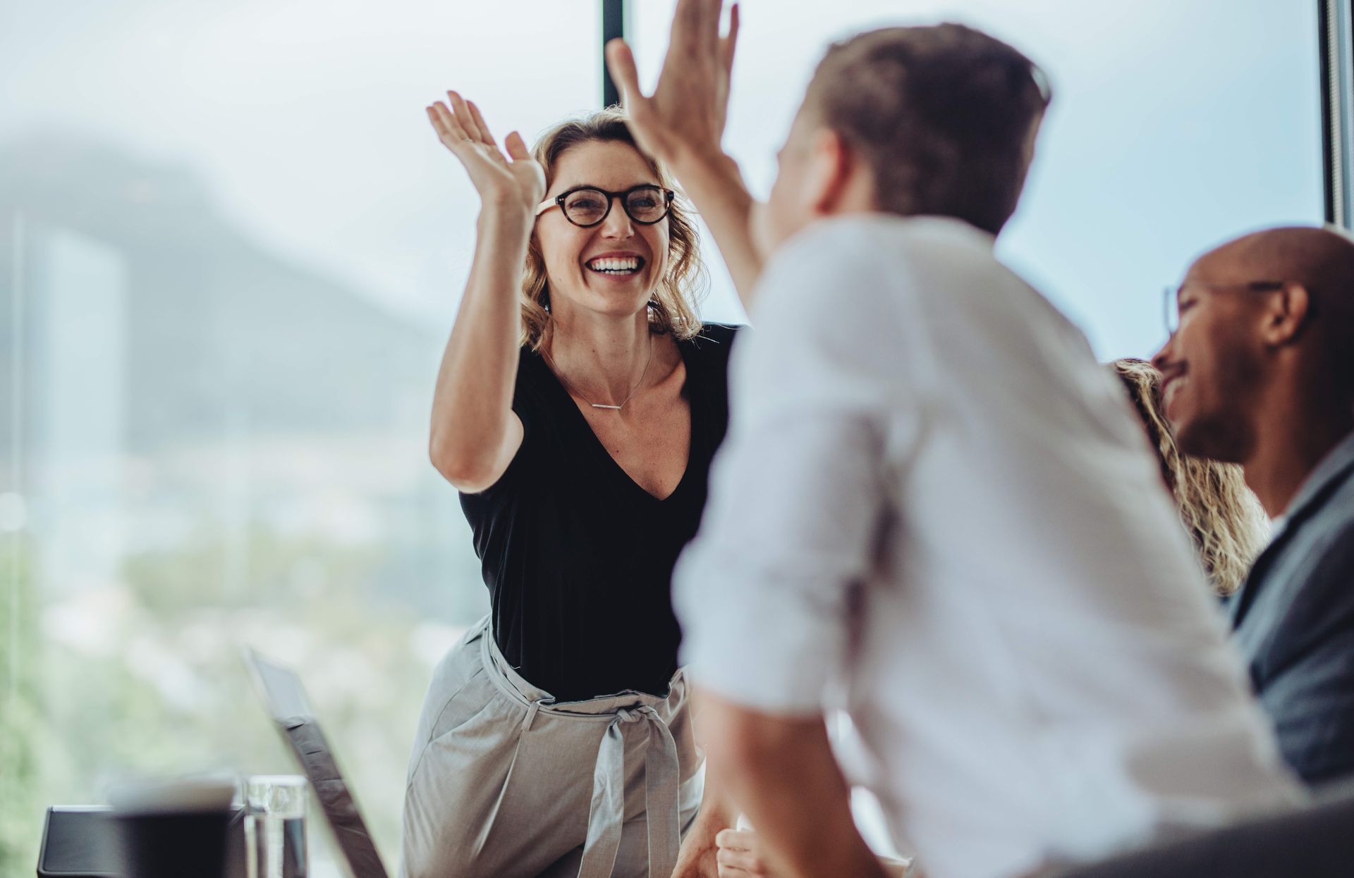 Colleagues celebrating in a bright office, smiling and high-fiving during a team meeting