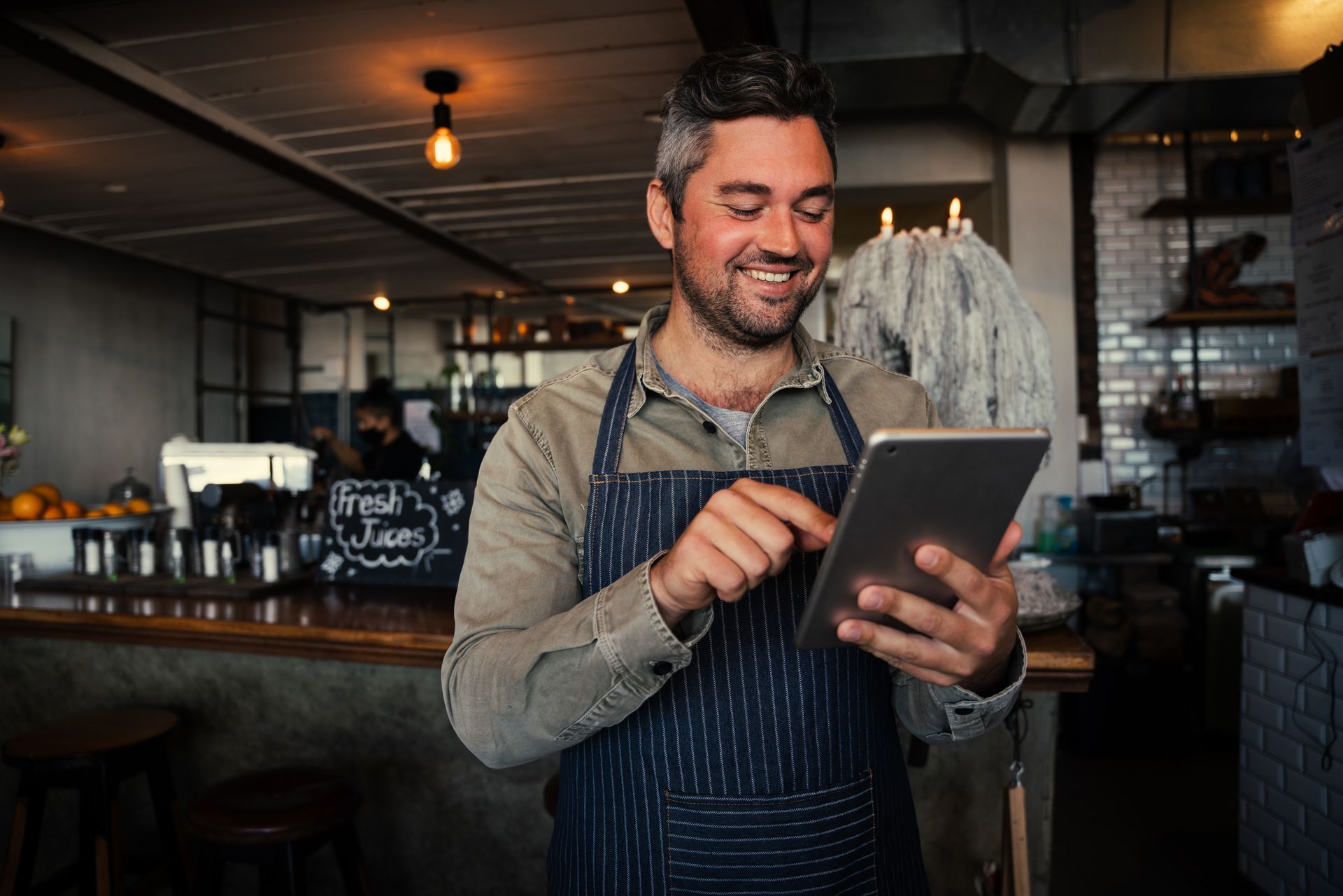 Smiling barista in apron using a tablet behind a coffee shop counter