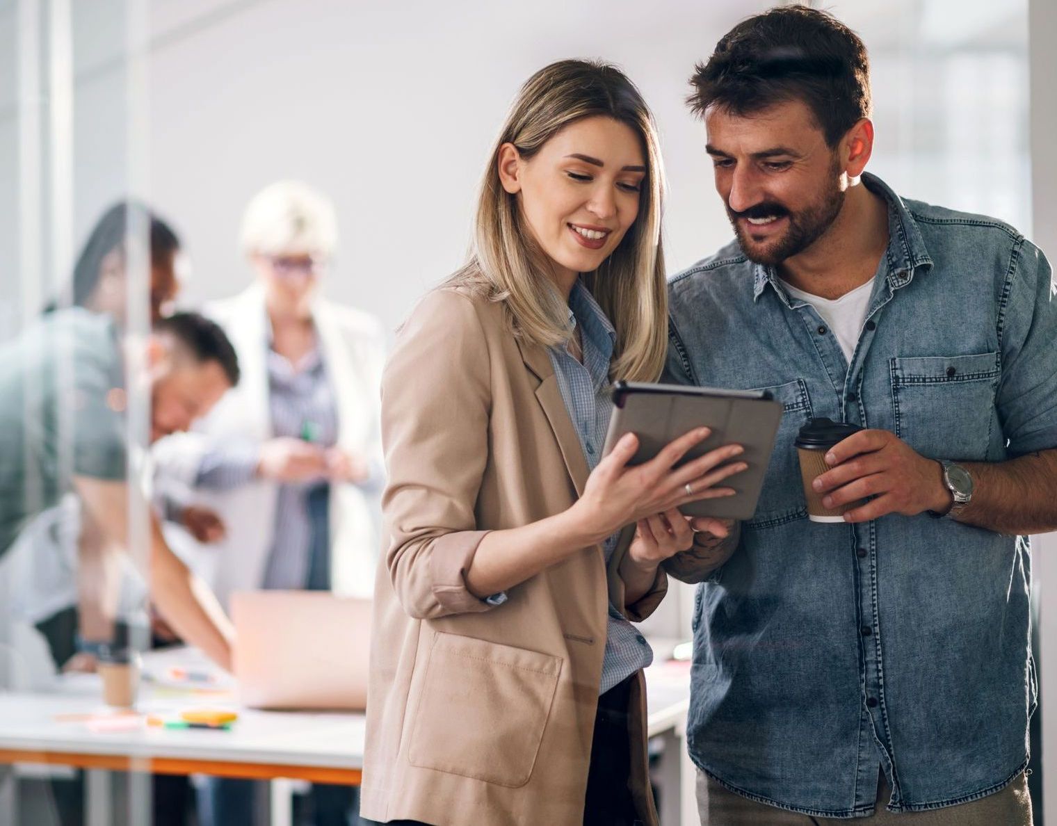 Two coworkers smiling and reviewing a tablet in a bright office