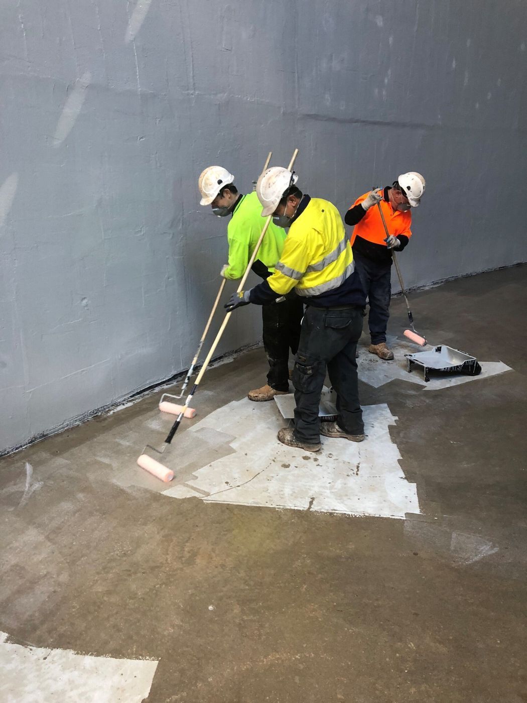 A group of men are painting a wall with rollers.