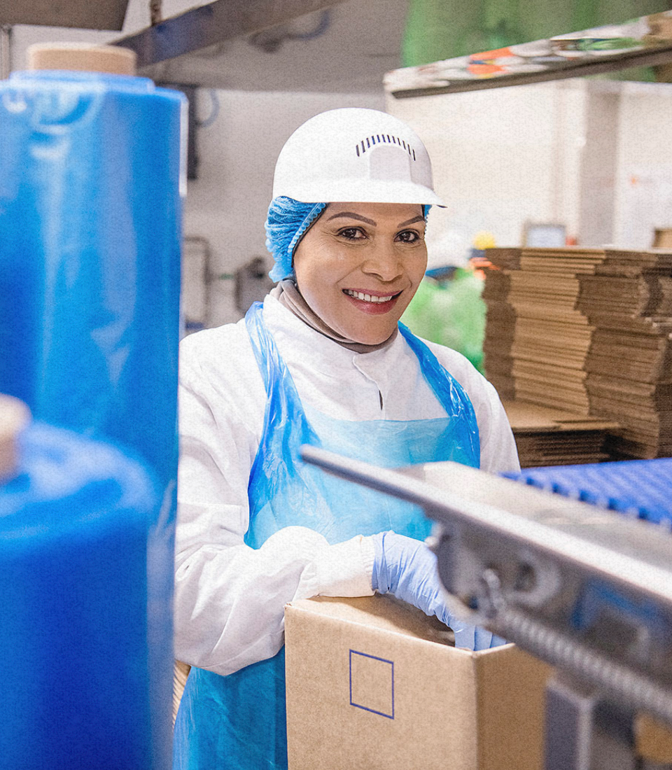 A woman wearing a mask and ear protectors is standing in a factory.