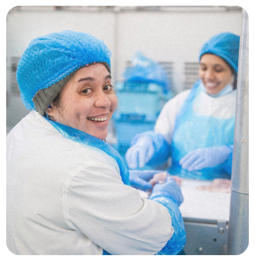 A woman wearing a mask and ear muffs is standing in a factory.