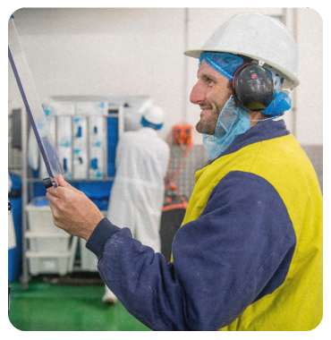 A woman wearing a mask and ear muffs is standing in a factory.