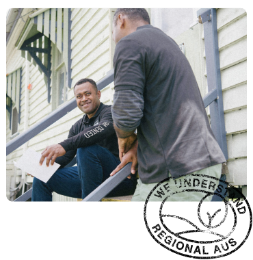 Two men in casual workwear sit on outdoor steps, engaged in conversation, with one holding a document and smiling.