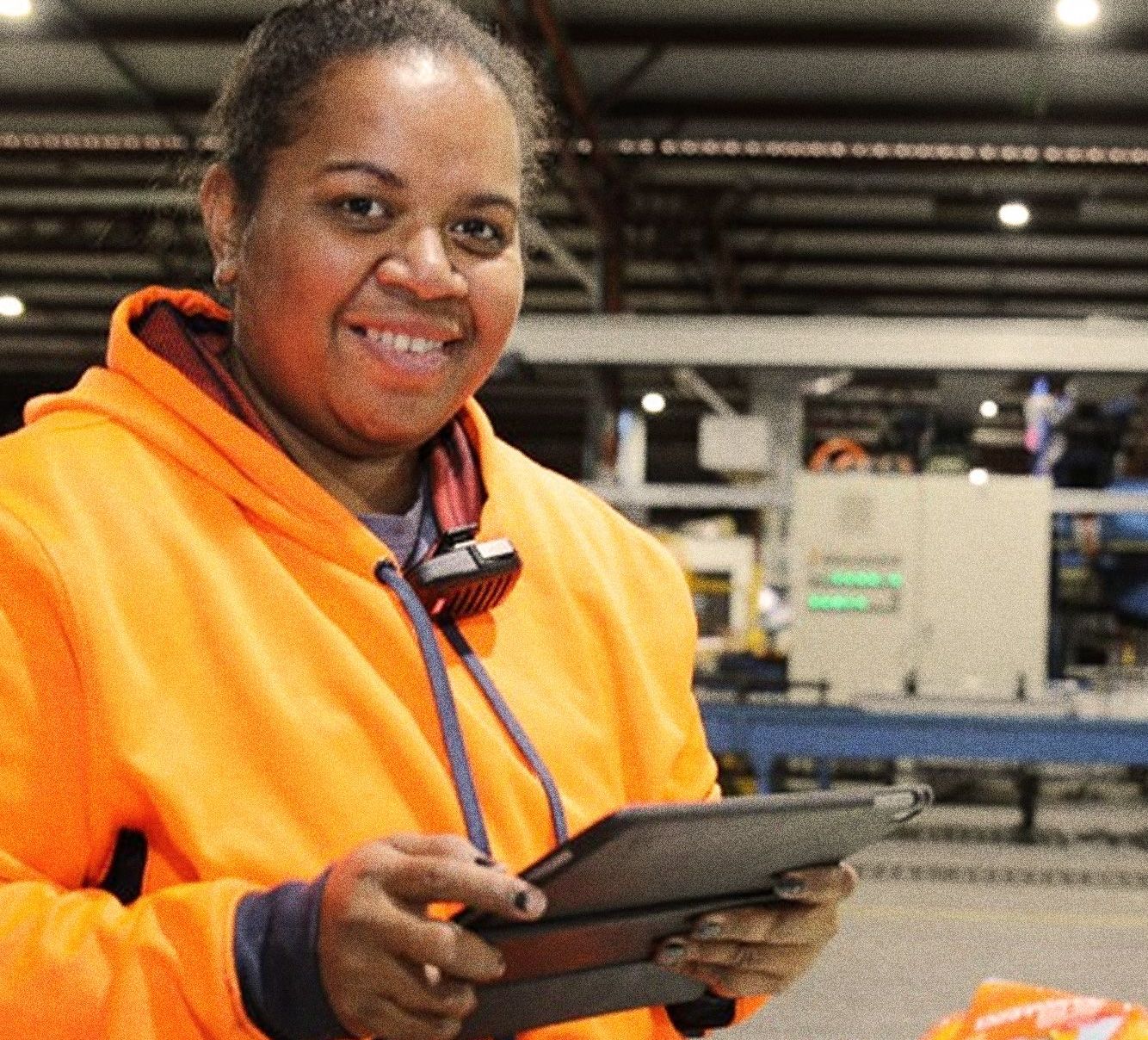 A woman in an orange hoodie is holding a tablet and smiling.
