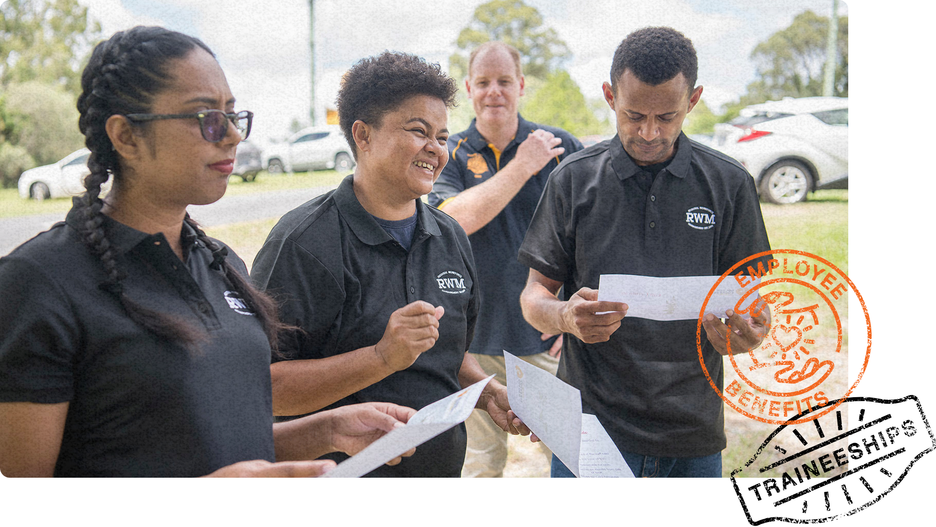 A group of workers in black RWM shirts review certificates outdoors, with one smiling and engaging in conversation.