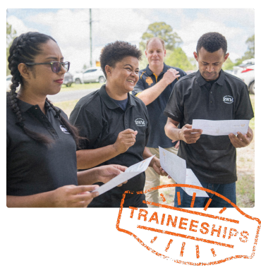 A group of workers in black RWM shirts review certificates outdoors, with one smiling and engaging in conversation.
