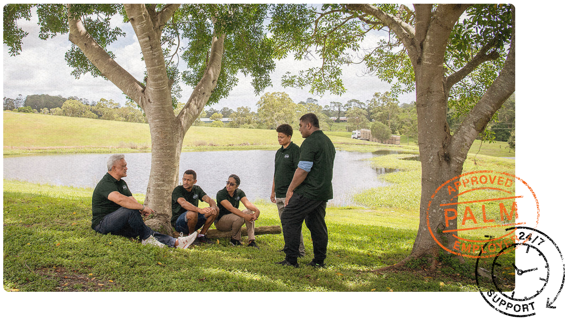 Five PALM scheme workers in green shirts sit and stand under a tree by a pond, engaged in conversation. 'Approved PALM Employer' stamp in the corner.