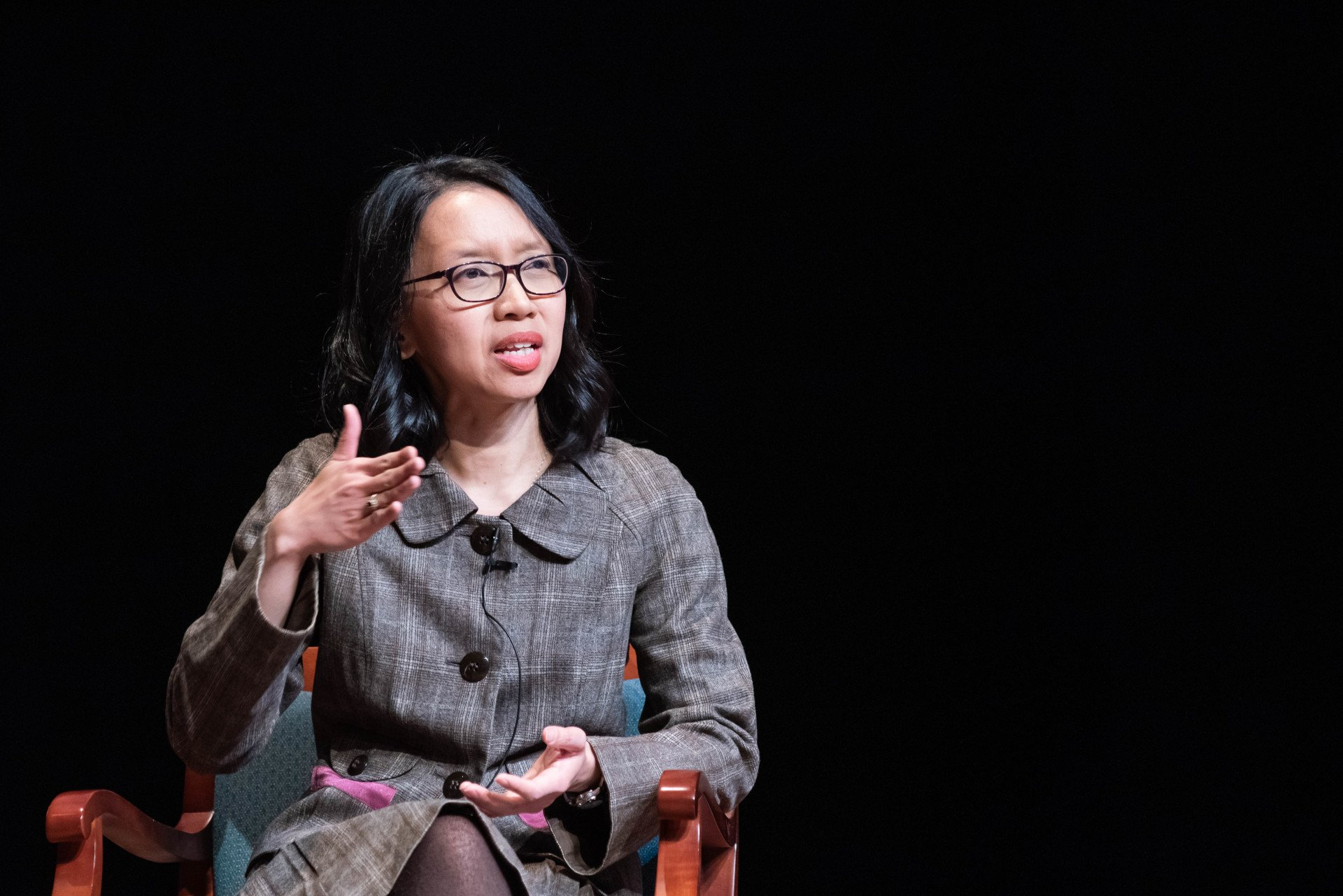 A woman wearing glasses is sitting in a chair and talking.