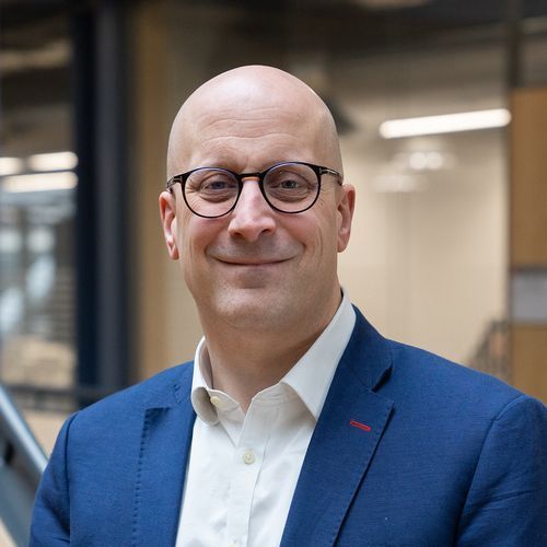 A bald man wearing glasses and a blue suit is smiling for the camera.