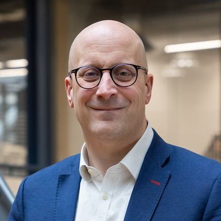 A bald man wearing glasses and a blue suit is smiling for the camera.