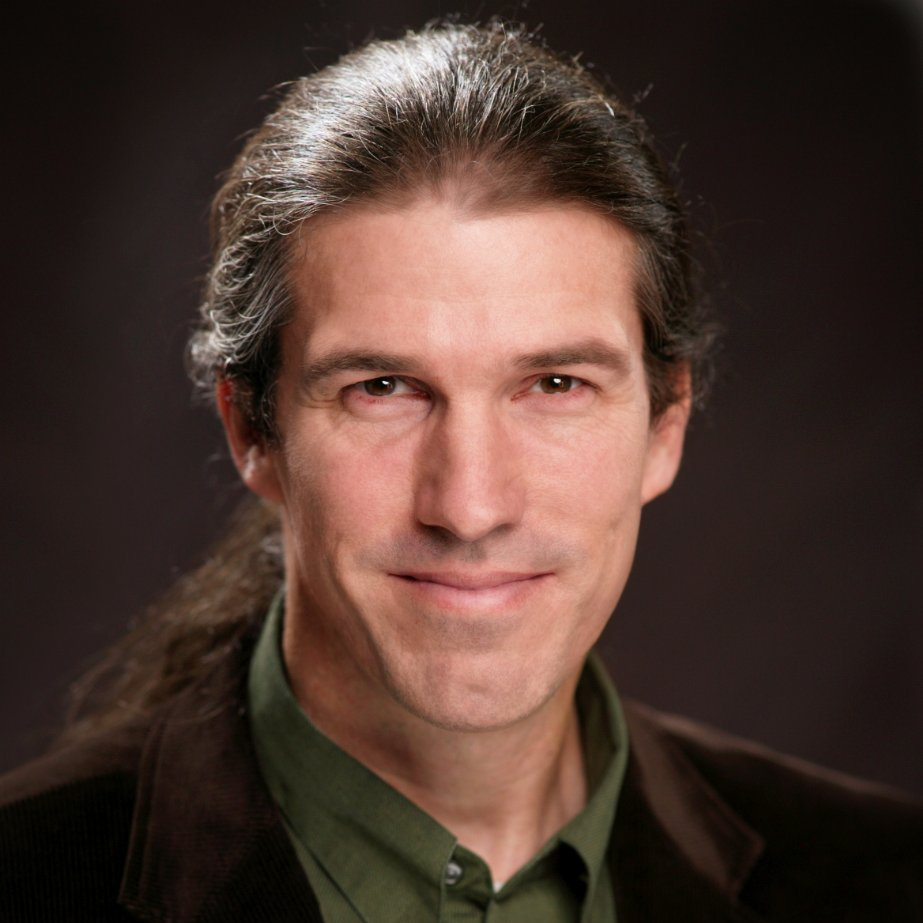 A man with long hair is wearing a green shirt and a brown jacket