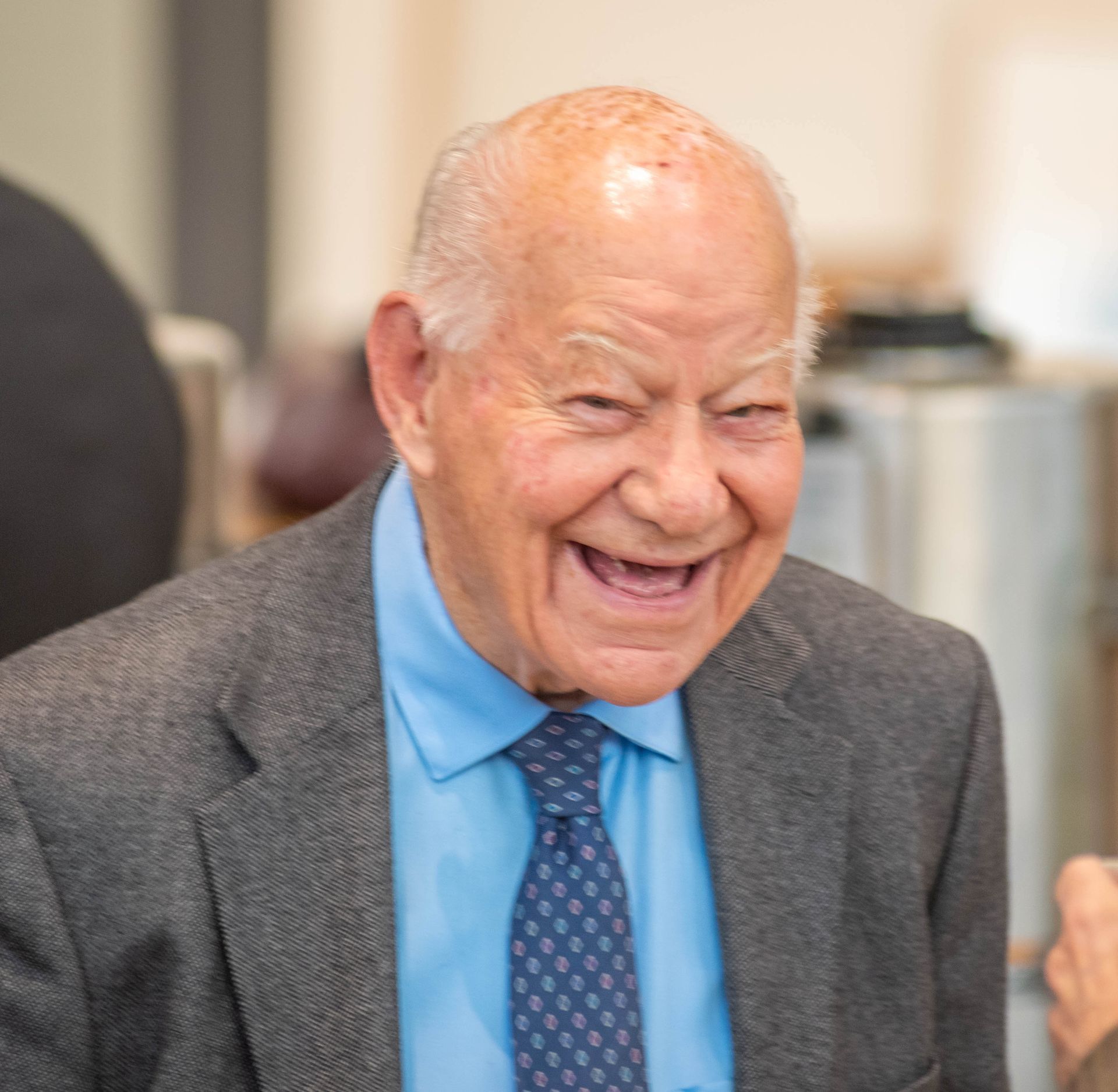 An older man in a suit and tie is smiling.