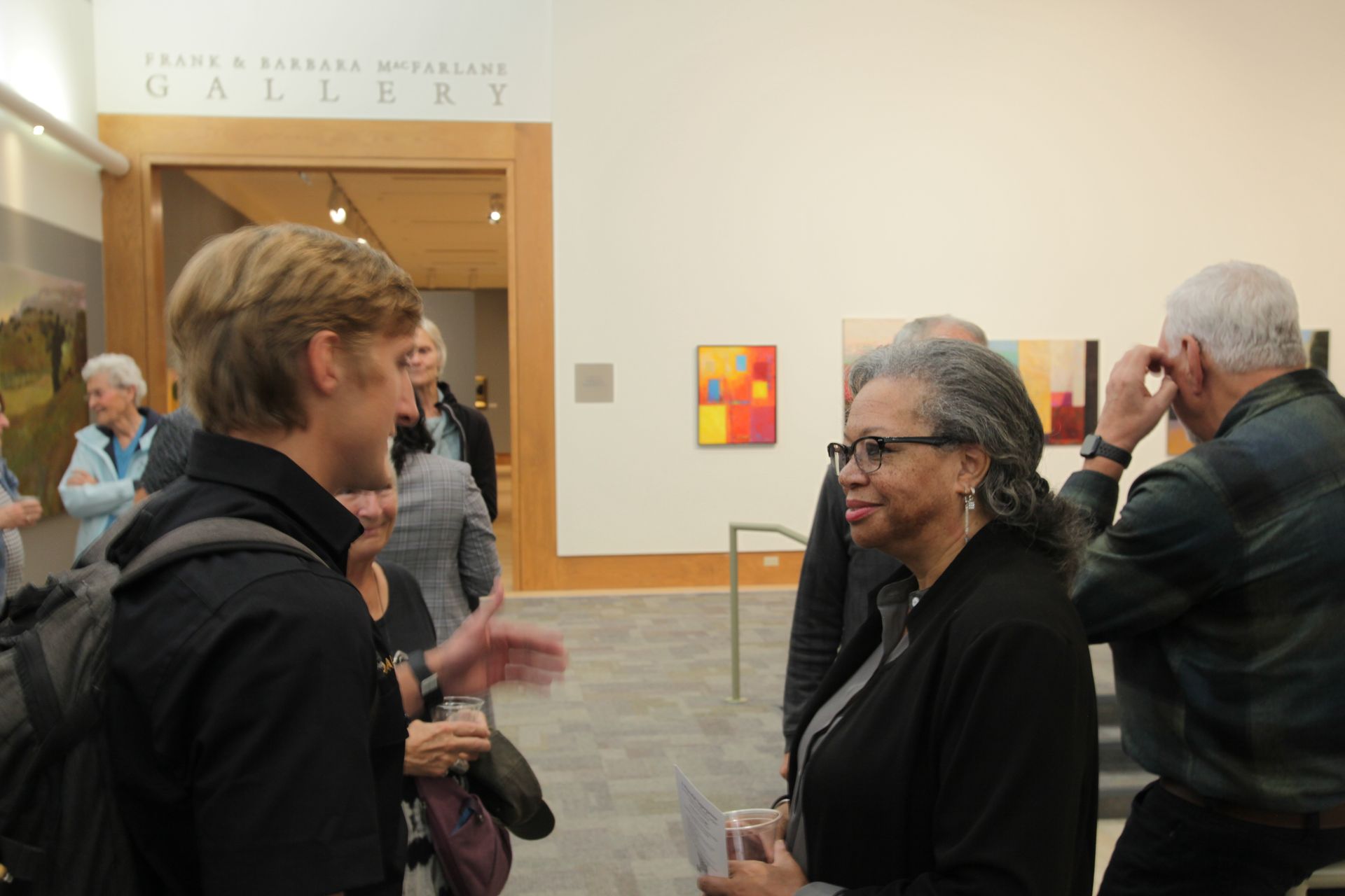 A group of people are standing in a gallery talking to each other.