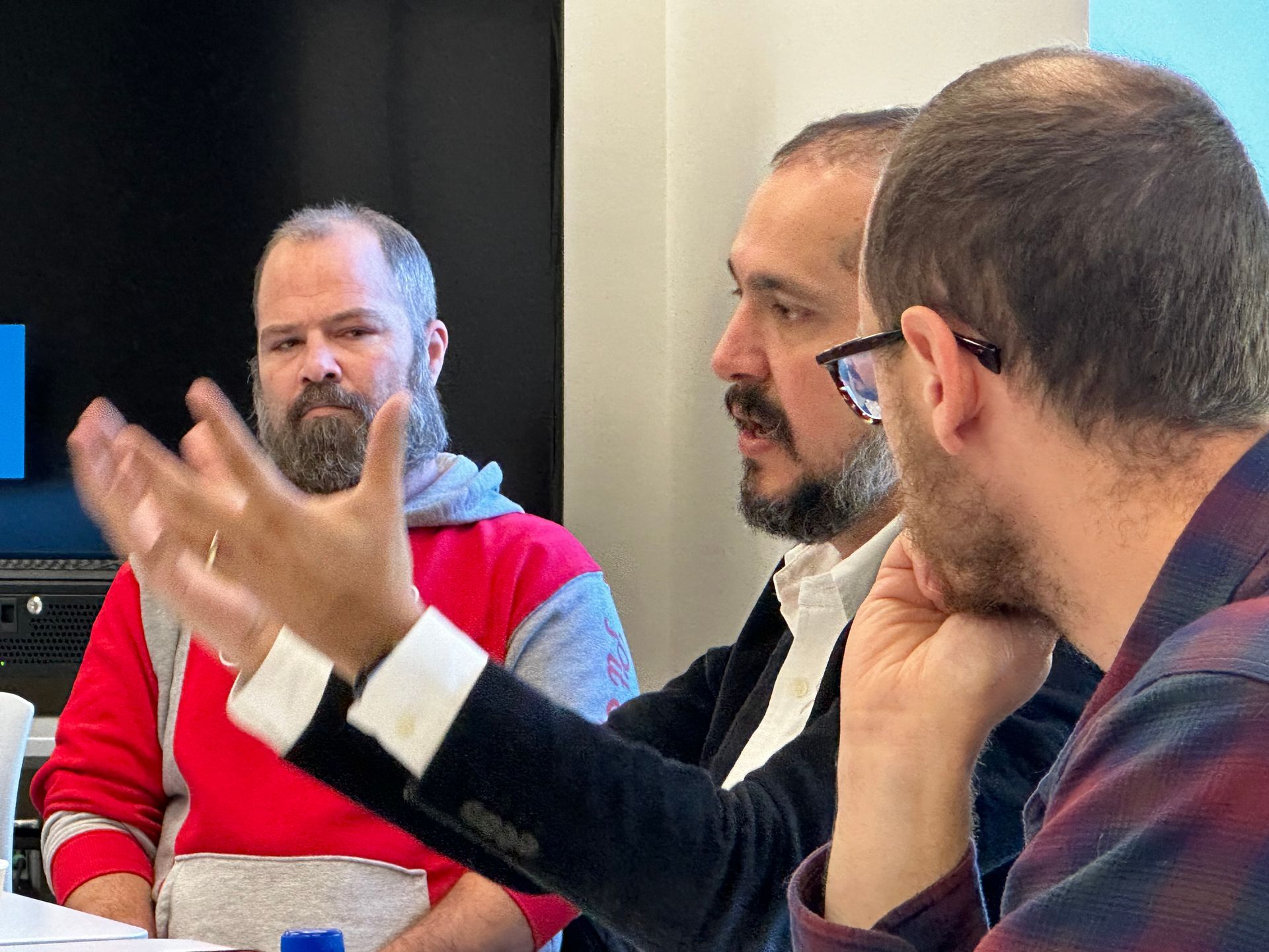 Three men are sitting at a table talking to each other.