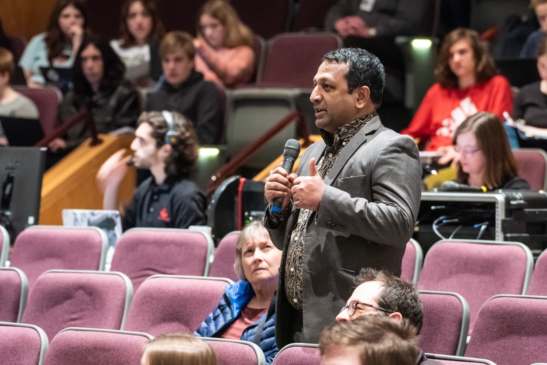 A man is holding a microphone in front of a crowd of people in an auditorium.