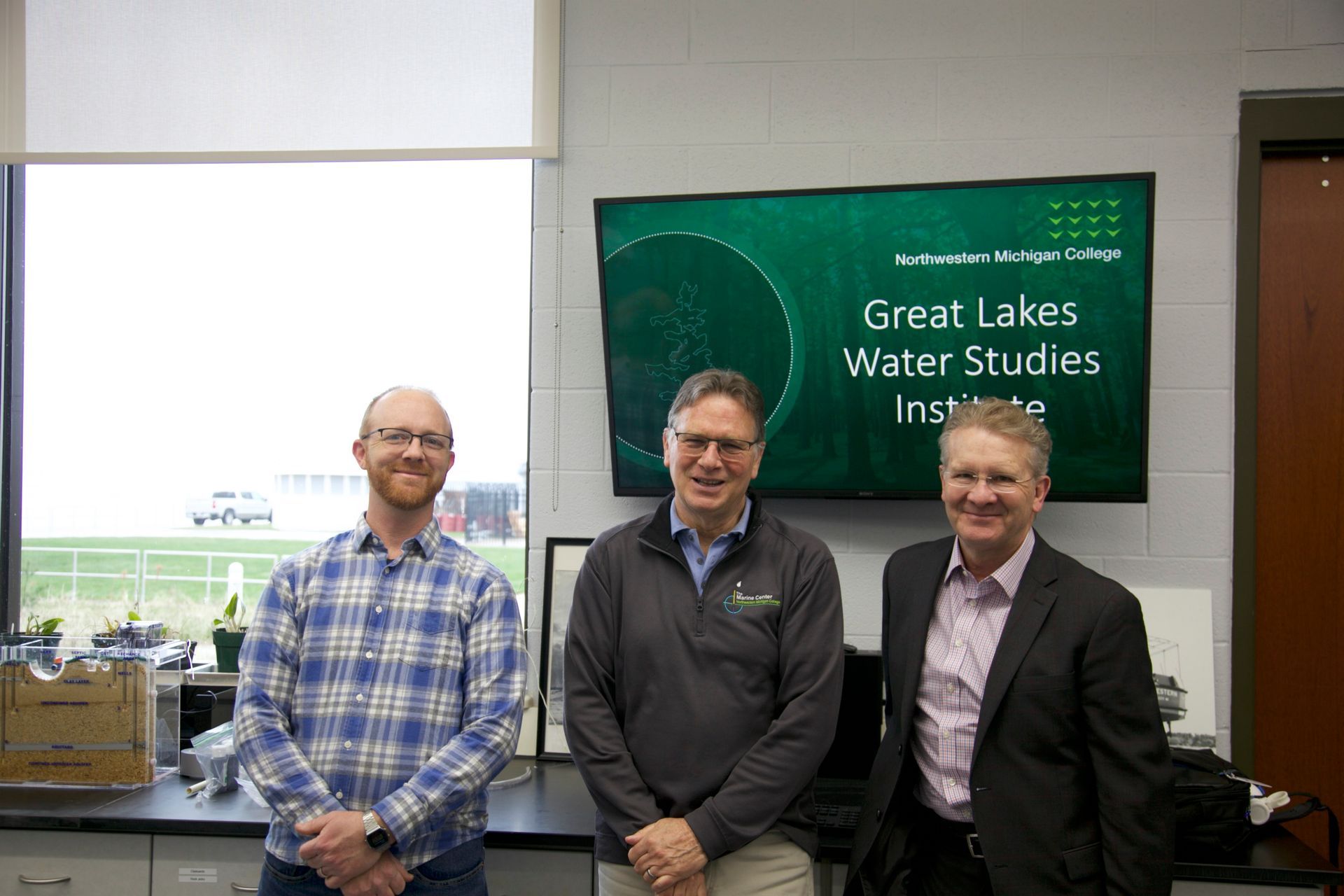 Three men are standing in front of a large screen that says great lakes water studies institute.