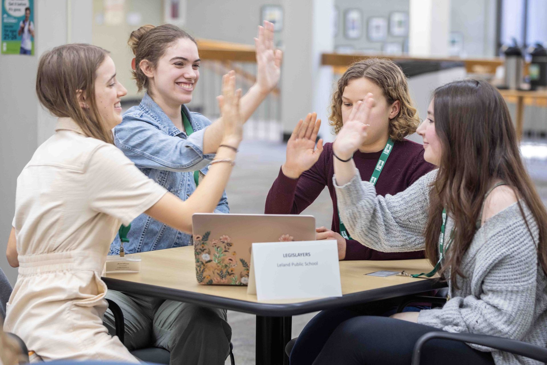 A group of young women are giving each other a high five while sitting at a table with laptops.