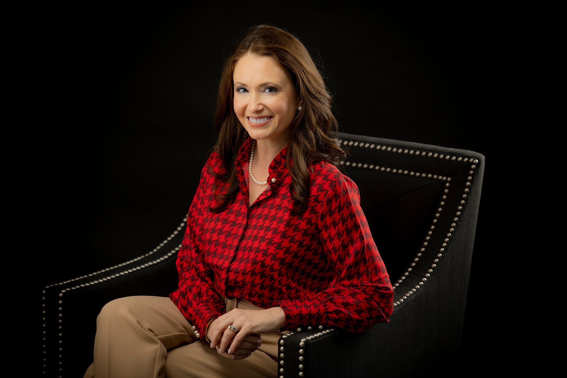 A woman is sitting in a chair wearing a red plaid shirt.
