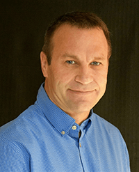 A man in a blue shirt is smiling for the camera.
