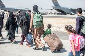 Travelers walking across an airport tarmac with luggage near parked airplanes