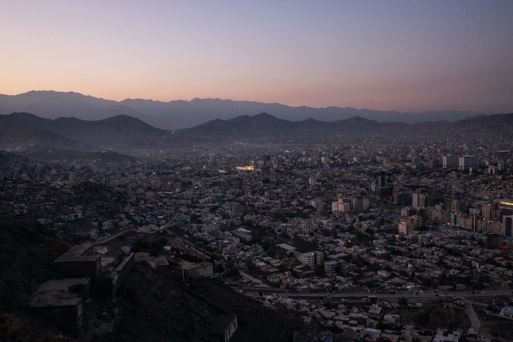 Dusk over a dense city in a mountain valley, with pink sky and distant hills.