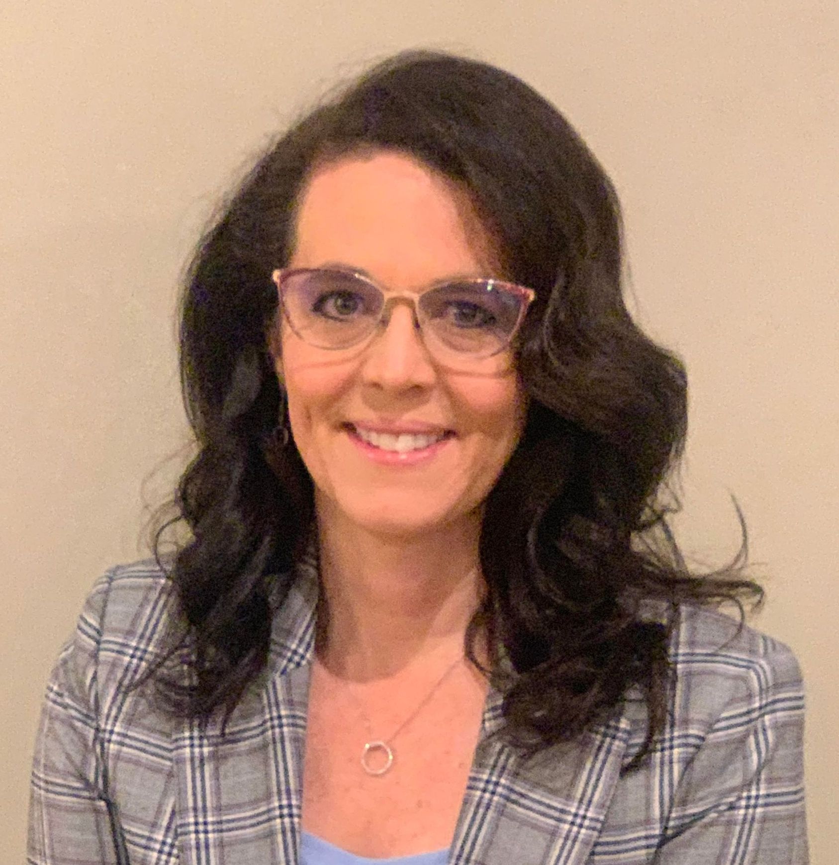 A woman wearing glasses and a plaid jacket is smiling for the camera.