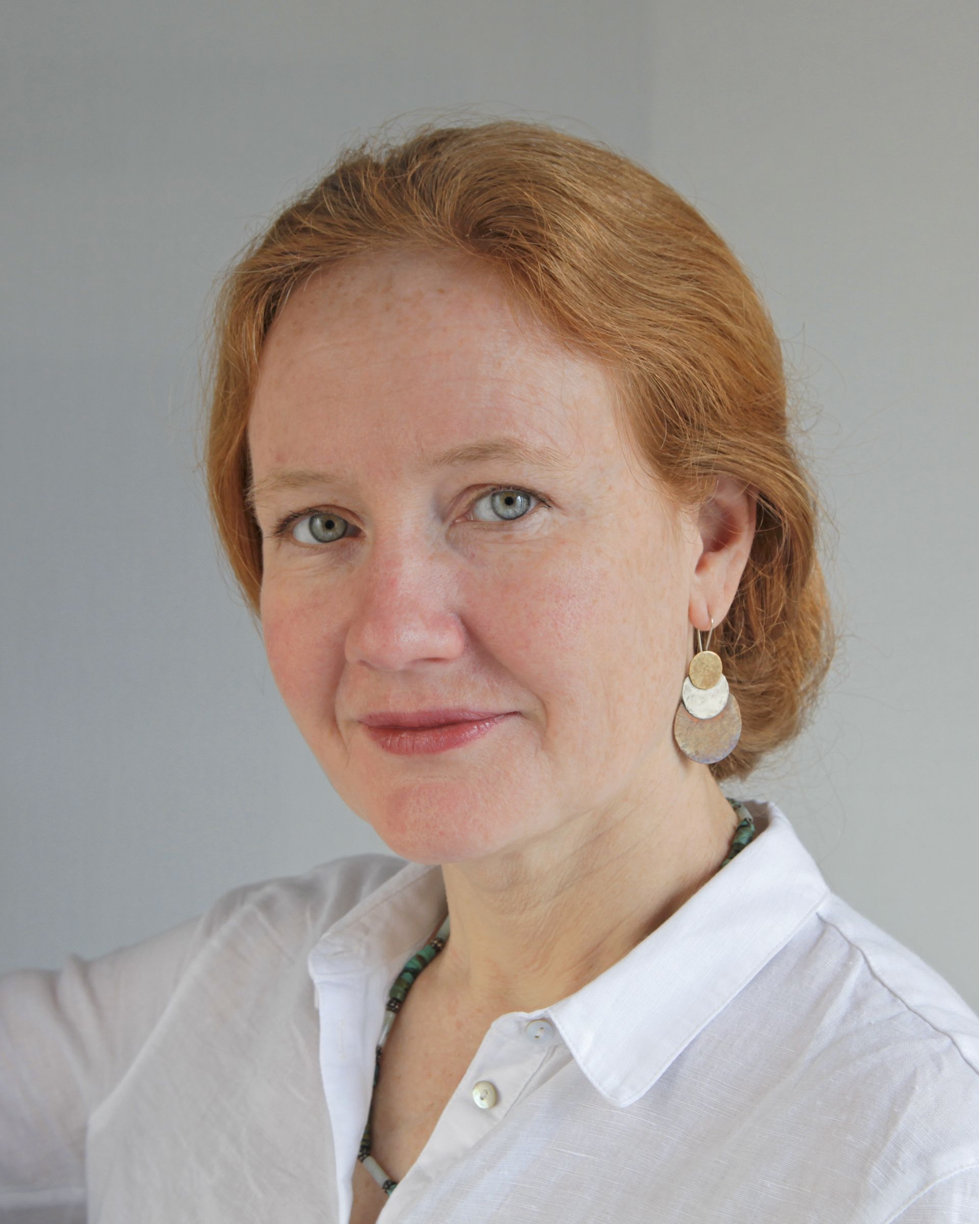 A woman with red hair is wearing a white shirt and earrings