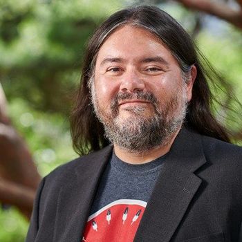 A man with long hair and a beard is wearing a suit and a watermelon shirt.