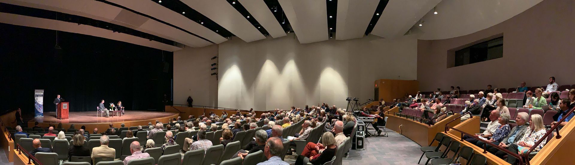 A large auditorium filled with people sitting in chairs and standing in front of a stage.