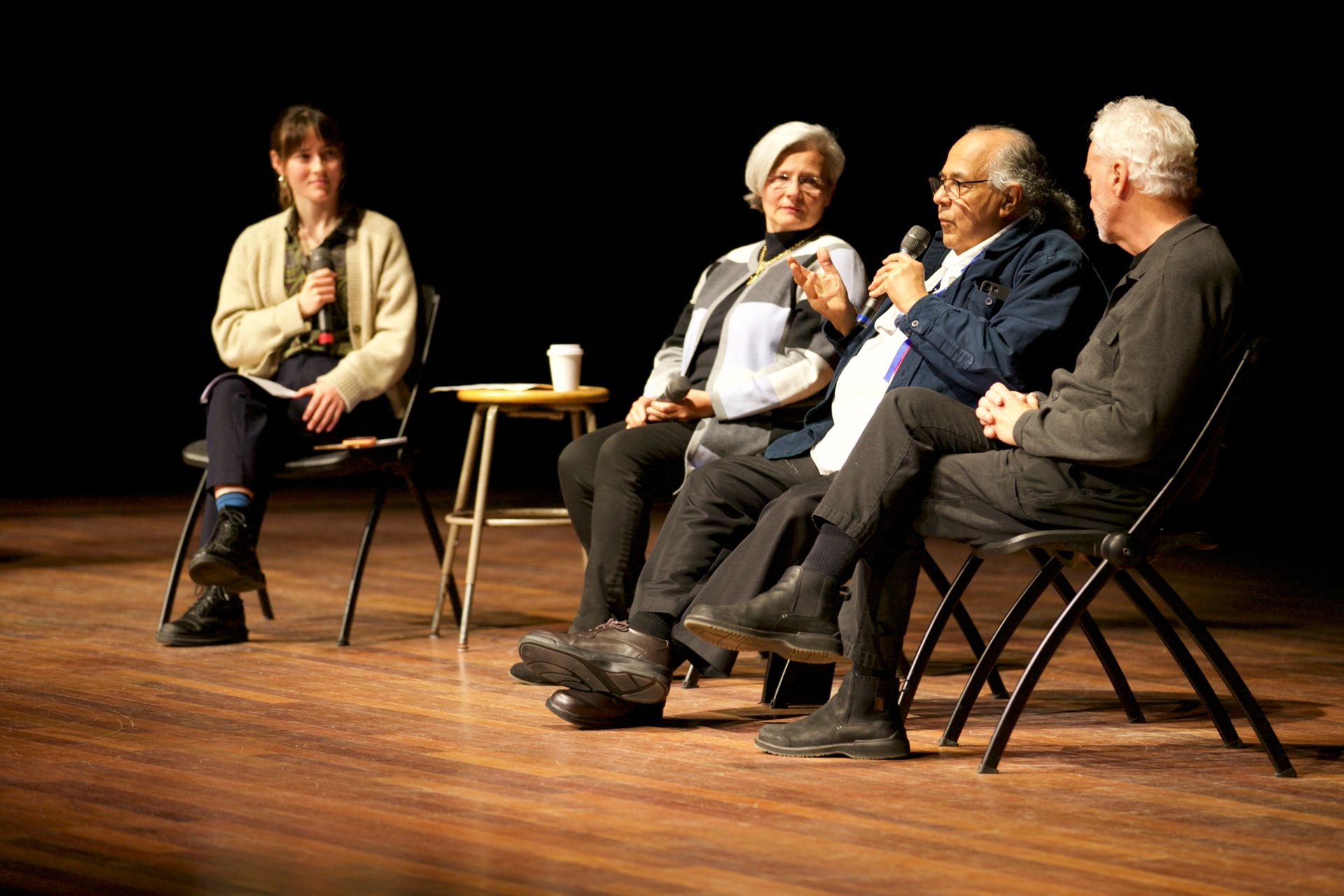 A group of people are sitting in chairs on a stage talking into microphones.