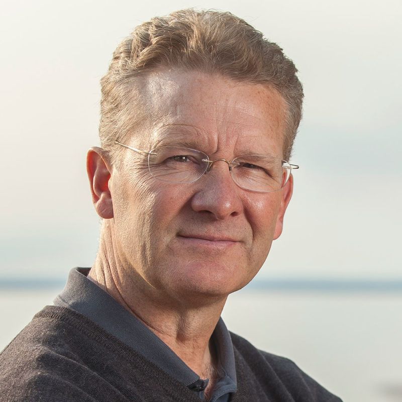 A man wearing glasses and a sweater looks at the camera
