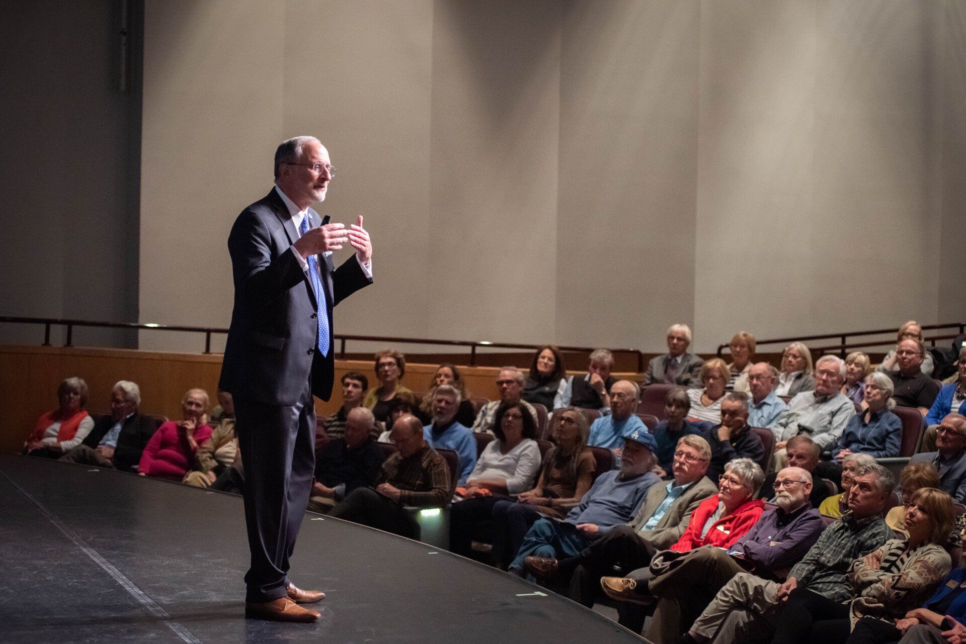 A man in a suit is standing on a stage in front of a crowd of people.