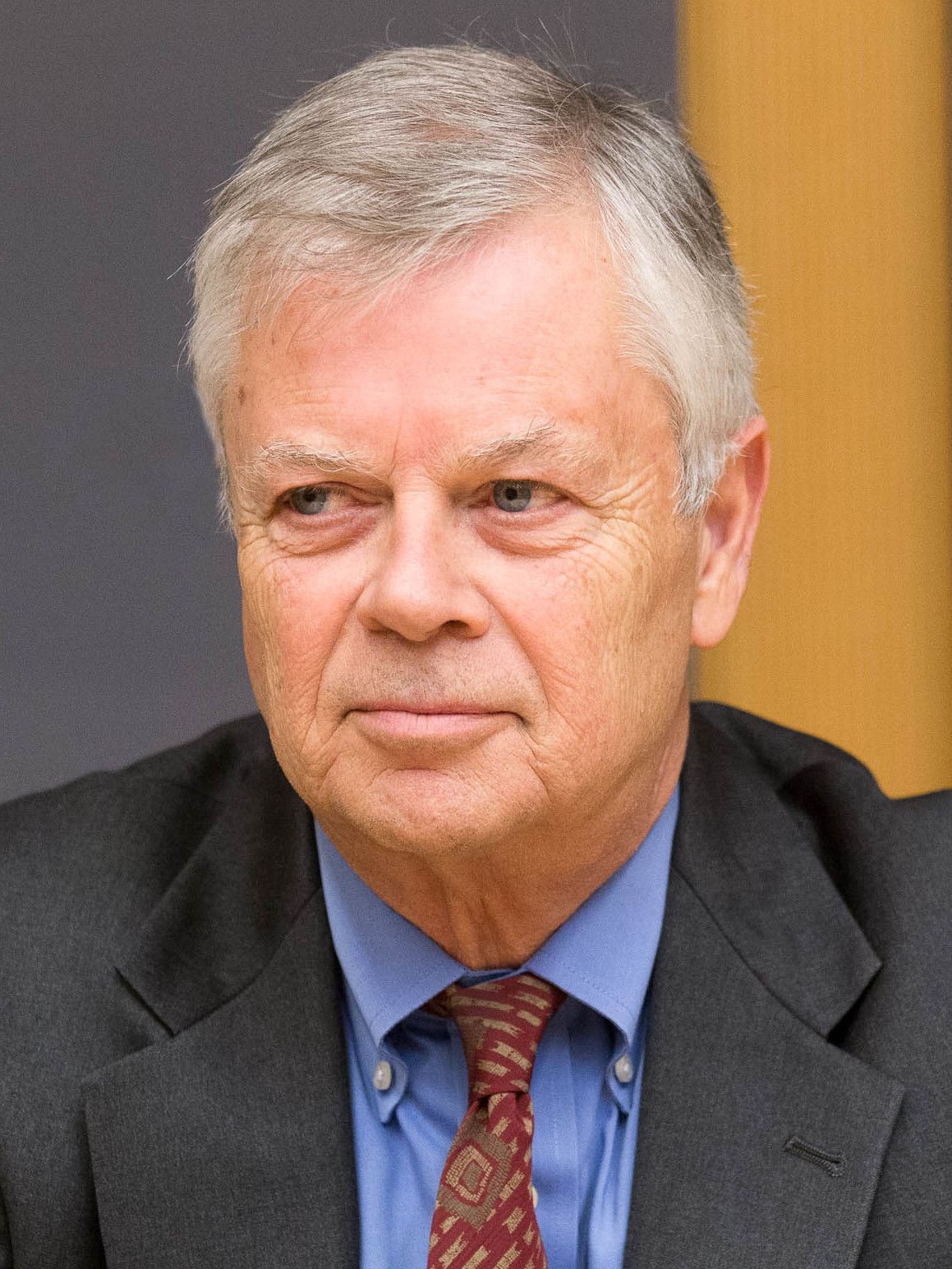Portrait of a gray-haired man in a suit and blue shirt, looking slightly to the side