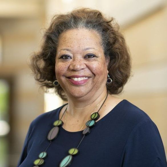 A woman wearing a blue shirt and a necklace smiles for the camera