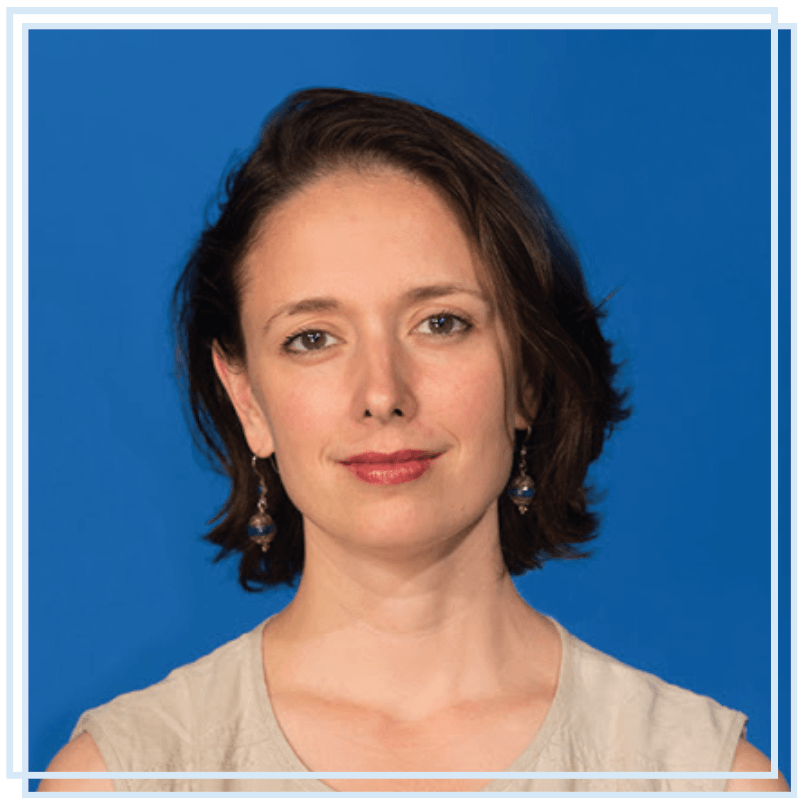 A woman wearing earrings is standing in front of a blue background.