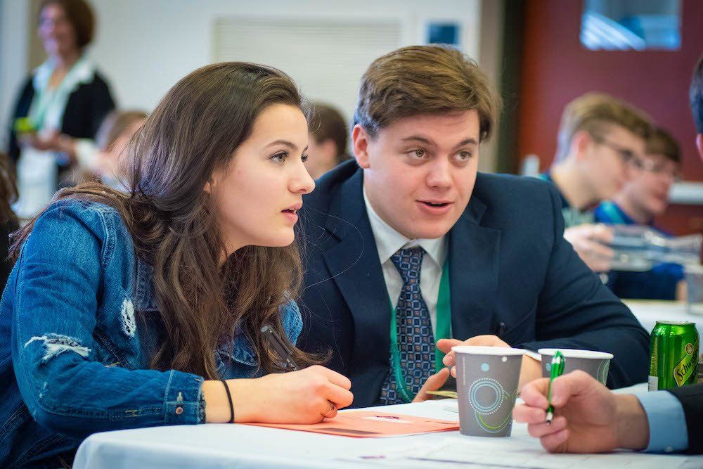 A man and a woman are sitting at a table talking to each other.