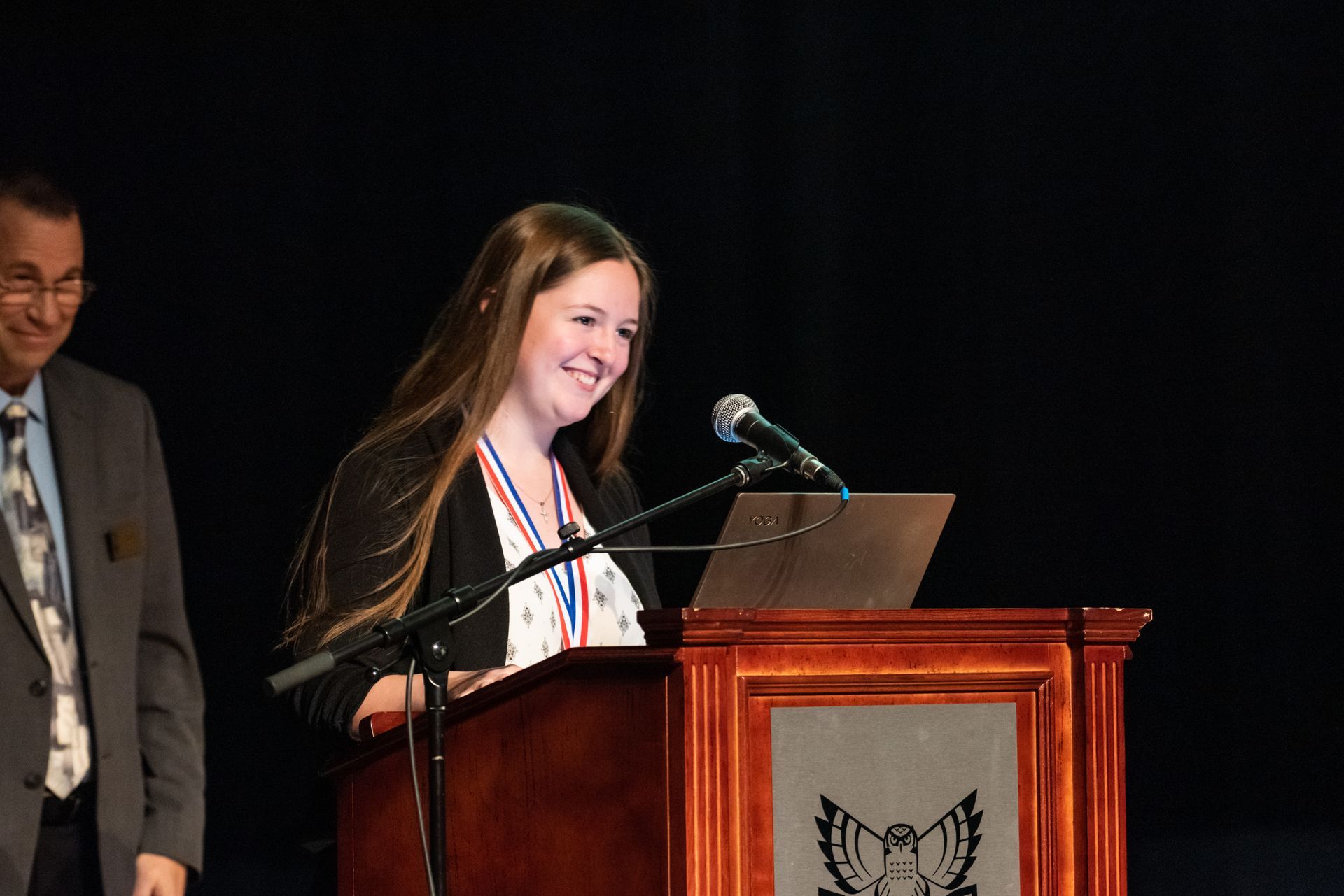 A woman is standing at a podium speaking into a microphone.
