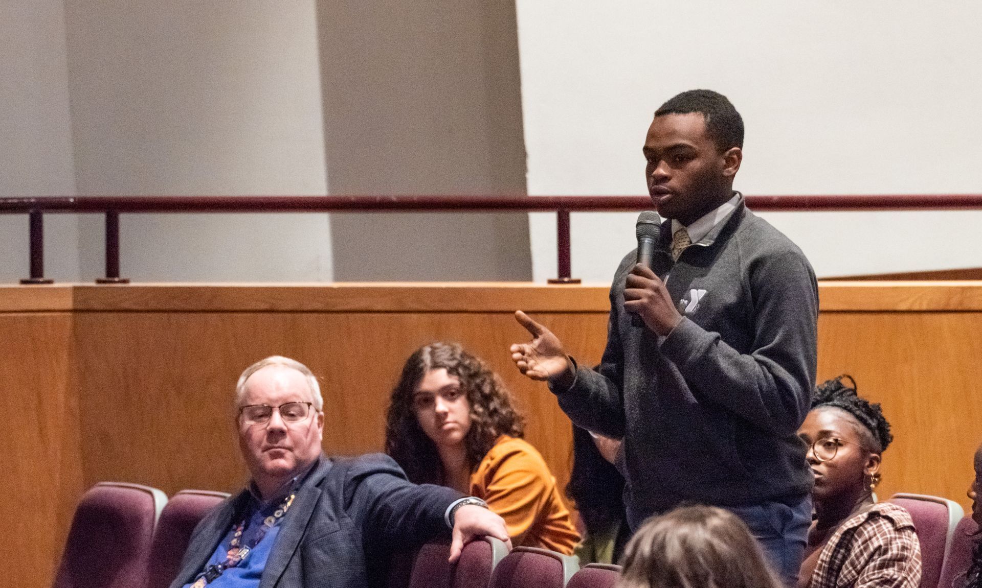 A man is speaking into a microphone in front of a group of people in an auditorium.