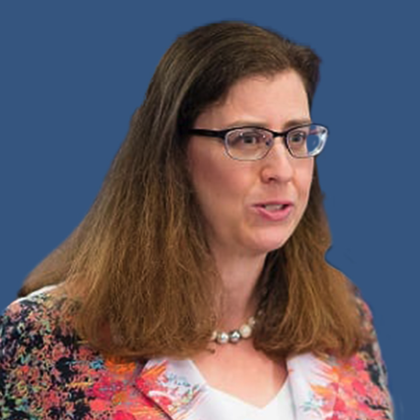 A woman wearing glasses and a floral jacket is standing in front of a blue background.
