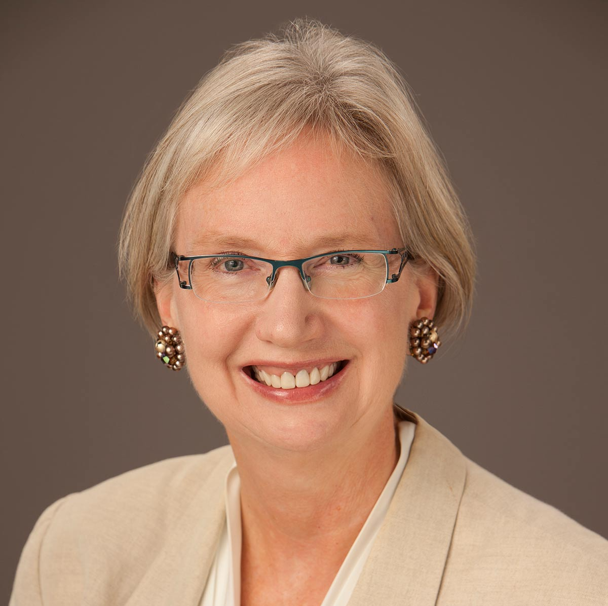 A woman wearing glasses and earrings smiles for the camera