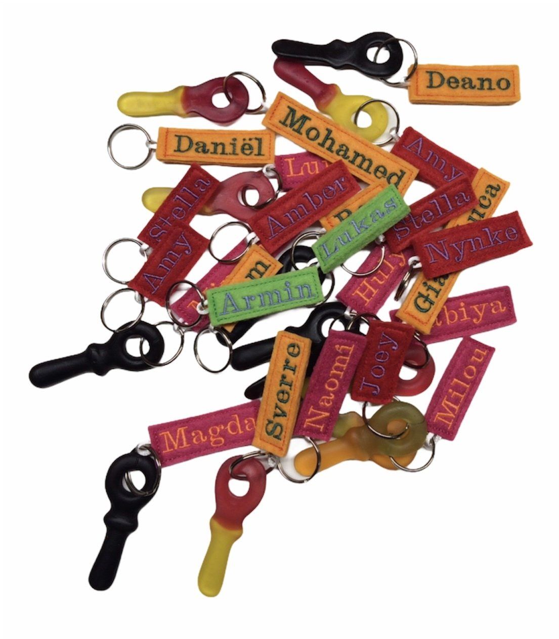 Een verzameling kleurrijke, gepersonaliseerde sleutelhangers met namen, op een witte achtergrond.
