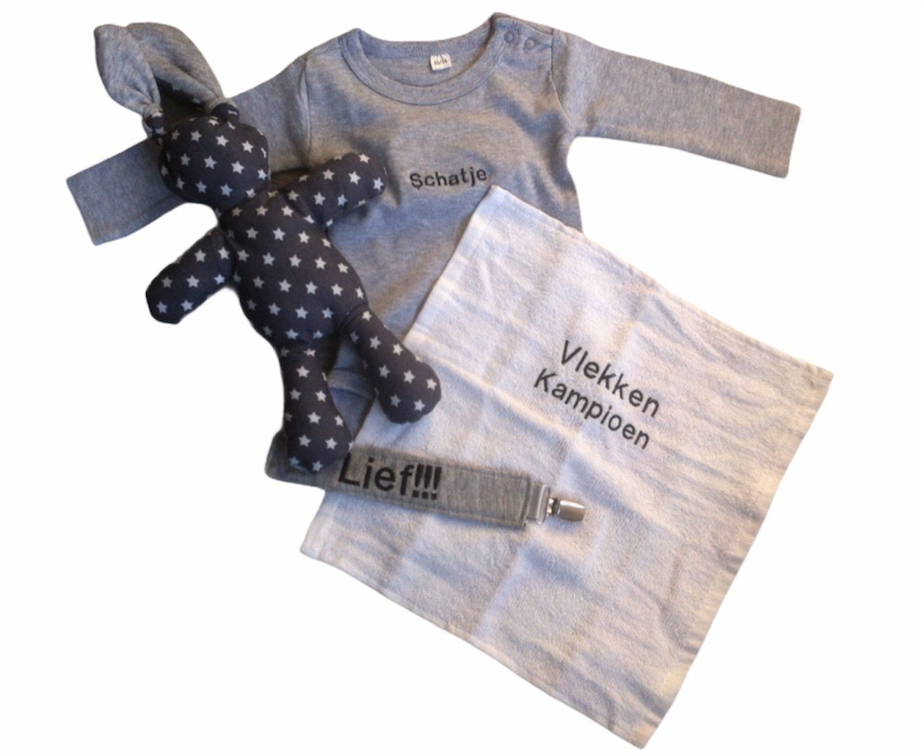 Grijze babykleertjes en een zwarte knuffelbeer met stippen liggen uitgestald op een witte achtergrond.