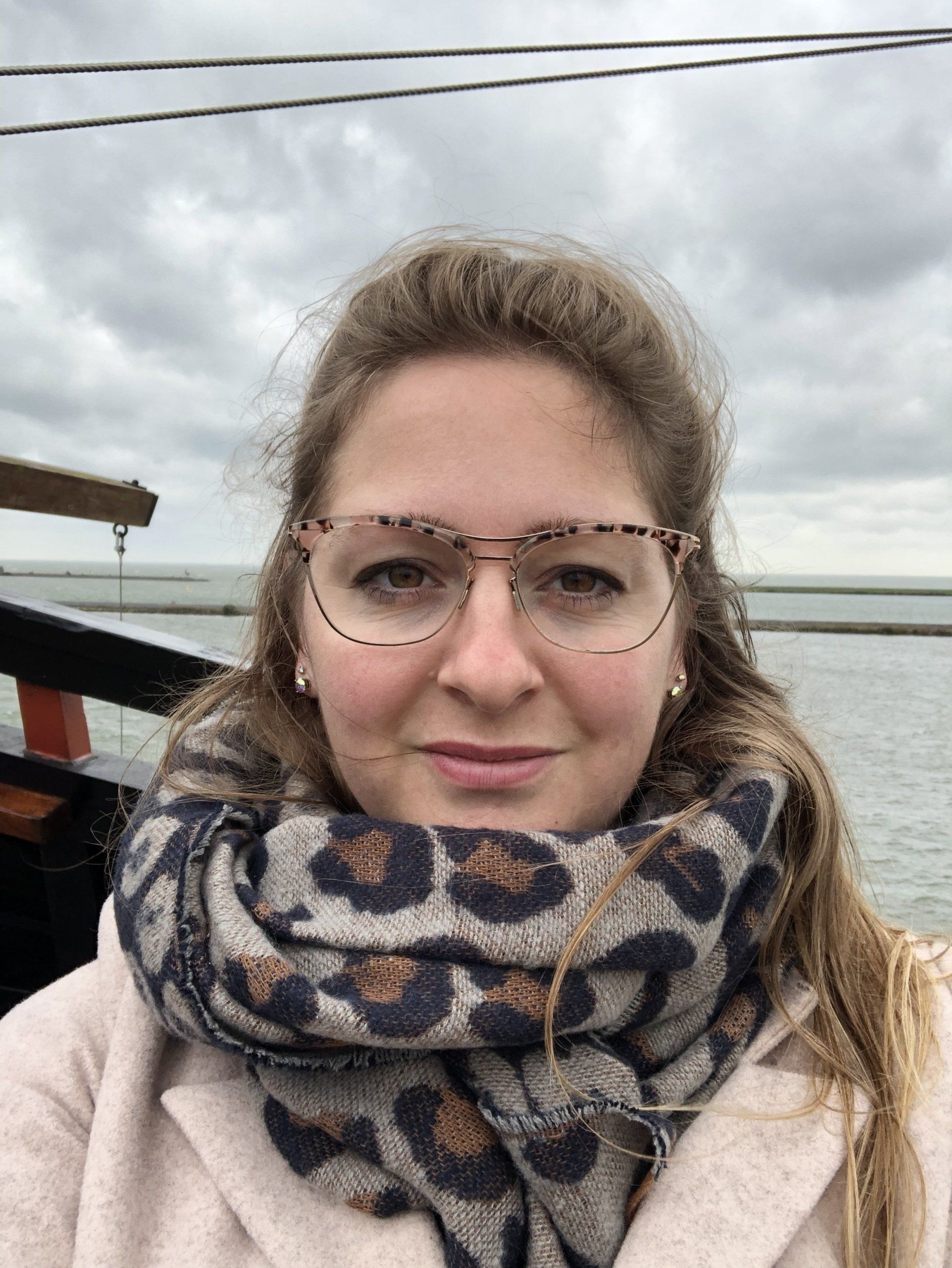 Persoon met bril en sjaal met patroon buiten op een bewolkte dag.
