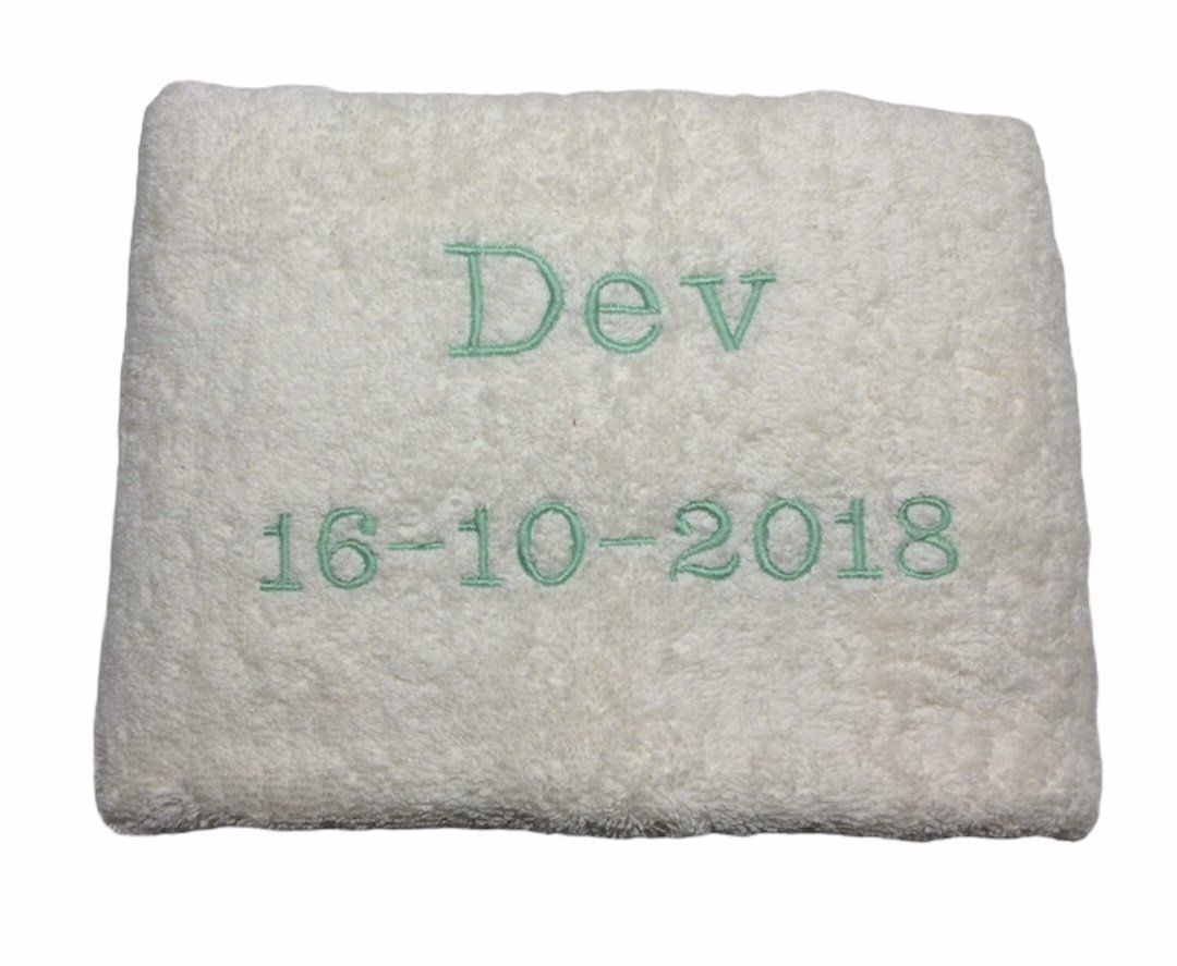 Wit kussen met turquoise borduurwerk waarop “Dev” en “16-10-2018” staan.